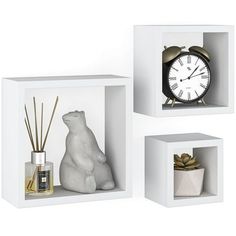 three white cubes with various items in them including a bear, an alarm clock and some plants