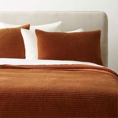 a bed with two pillows and an orange blanket