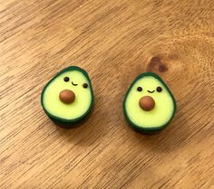 two slices of avocado with faces painted on them sitting on a wooden surface