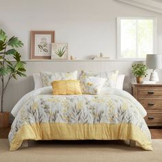 a bed with yellow and white comforters in a bedroom next to a window, potted plant and dresser