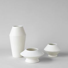 three white vases sitting next to each other on a gray surface, one is empty