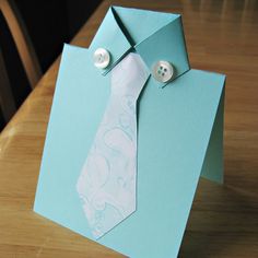 an origami tie on top of a blue card with buttoned up buttons