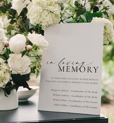 a memorial sign sitting on top of a table with white flowers in vases next to it