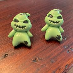 two green toy figures sitting on top of a wooden table