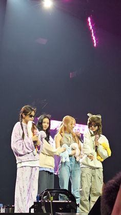 group of people standing on stage with microphones in their hands and one person holding something