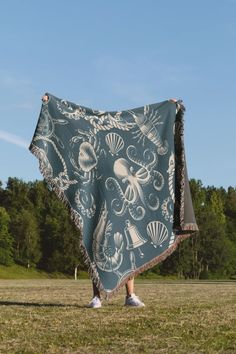 a person standing in a field holding up a blanket with an octopus design on it