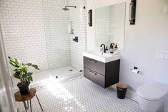 a white tiled bathroom with black accents and plants in the sink area, along with a walk - in shower