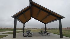 an empty picnic area with tables and benches under a covered structure on a cloudy day