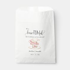 a white bag with the words tea and flowers on it, sitting next to a cup