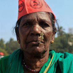 an old woman wearing a red hat and green shirt with gold jewelry on her nose