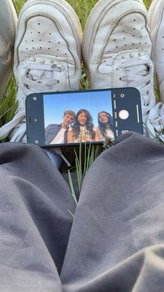 someone is taking a photo with their cell phone while sitting in the grass and wearing tennis shoes