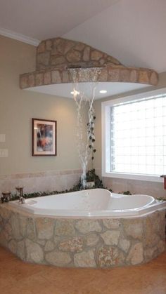 a large bath tub sitting under a window next to a stone wall with a waterfall coming out of it