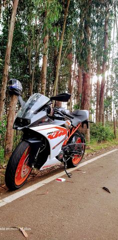 an orange and white motorcycle parked on the side of a road in front of trees