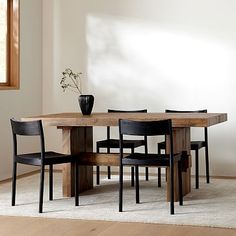 a dining table with four chairs and a vase on the top, in front of a white wall