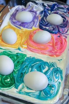 four eggs are sitting in the middle of an egg tray with colored icing on it