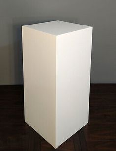 a tall white box sitting on top of a wooden table next to a wall and floor