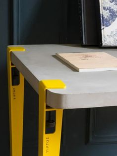 a table with two yellow legs and a book on top of it next to a painting