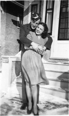 an old black and white photo of a man hugging a woman in front of a house