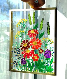 a person holding up a glass painting with flowers on it in front of a window