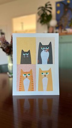 a card with four cats on it sitting on a table in front of a vase