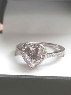 a heart shaped diamond ring sitting on top of a white box with diamonds around it