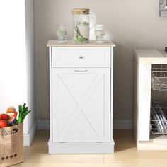 a white cabinet sitting next to a basket filled with fruits and vegetables on top of a hard wood floor