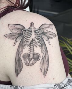 a woman's back with a skeleton and feathers tattoo on her upper arm,