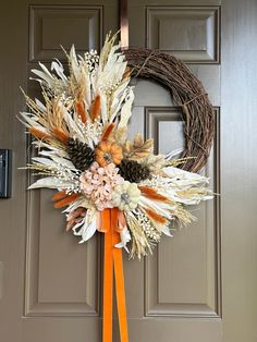 a wreath is hanging on the front door with an orange ribbon and flowers in it