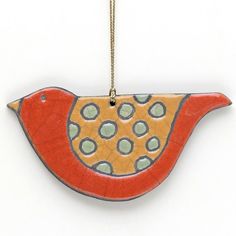 a ceramic bird ornament hanging from a gold chain on a white wall with polka dots