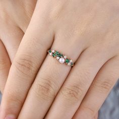 a woman's hand wearing a ring with three stones and emeralds on it