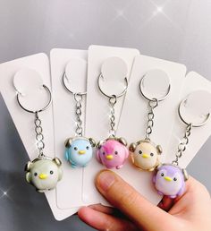 a hand holding four key chains with different colored birds on them and one has a white tag attached to it