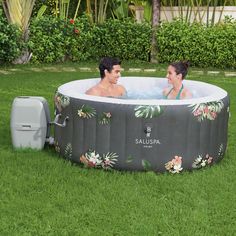 two people sitting in an inflatable hot tub on the grass near some bushes