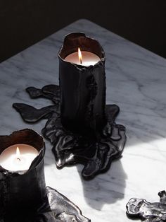 two black candles sitting on top of a marble table next to another candle in the middle