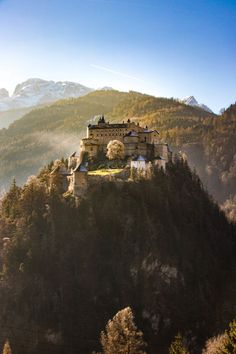 an old castle on top of a mountain in the middle of autumn with trees around it