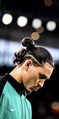 a male tennis player with a ponytail in his hair looking at his cell phone while standing on the court