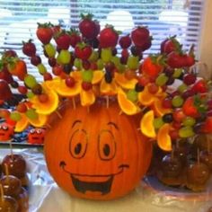 a pumpkin with fruit on it sitting in front of some candy apples and strawberries