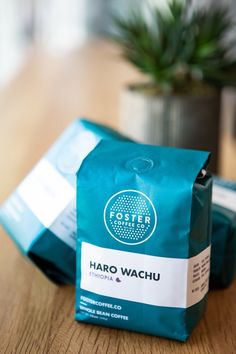 two bags of coffee sitting on top of a wooden table next to a potted plant