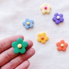 a hand is holding small plastic flowers on a white tablecloth with several colors and shapes