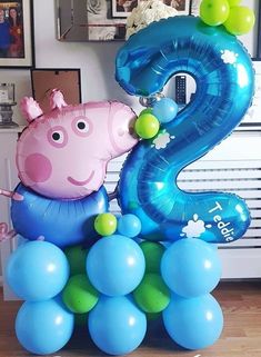 a number two balloon with a peppa pig sitting on top of some blue and green balloons