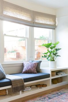 a window seat with pillows on it in front of a potted plant and rug