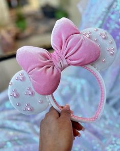 a hand holding a pink and white minnie mouse ears headband with pearls on it