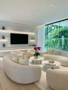 a living room filled with white furniture and a flat screen tv mounted on the wall