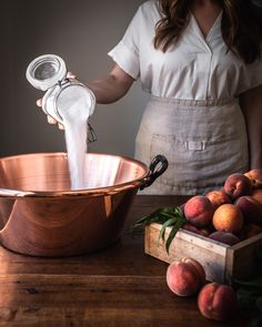 a woman pours milk into a copper bowl filled with peaches