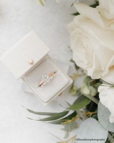 an engagement ring sitting in a box next to flowers and greenery on a white surface