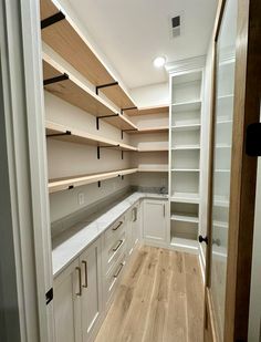 an empty walk in closet with white cabinets and wood flooring on the side wall