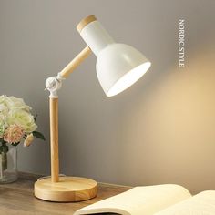 an open book on a desk next to a lamp and vase with flowers in it