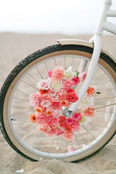 a white bicycle with flowers on the front wheel is parked in the sand at the beach