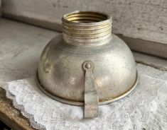 an old silver vase sitting on top of a white lace covered table cloth with a pair of scissors stuck in it