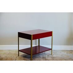 a red and gold end table with one shelf on the bottom, against a white wall