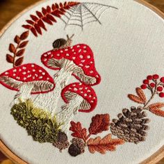 a close up of a embroidery on a piece of cloth with leaves and mushrooms in it